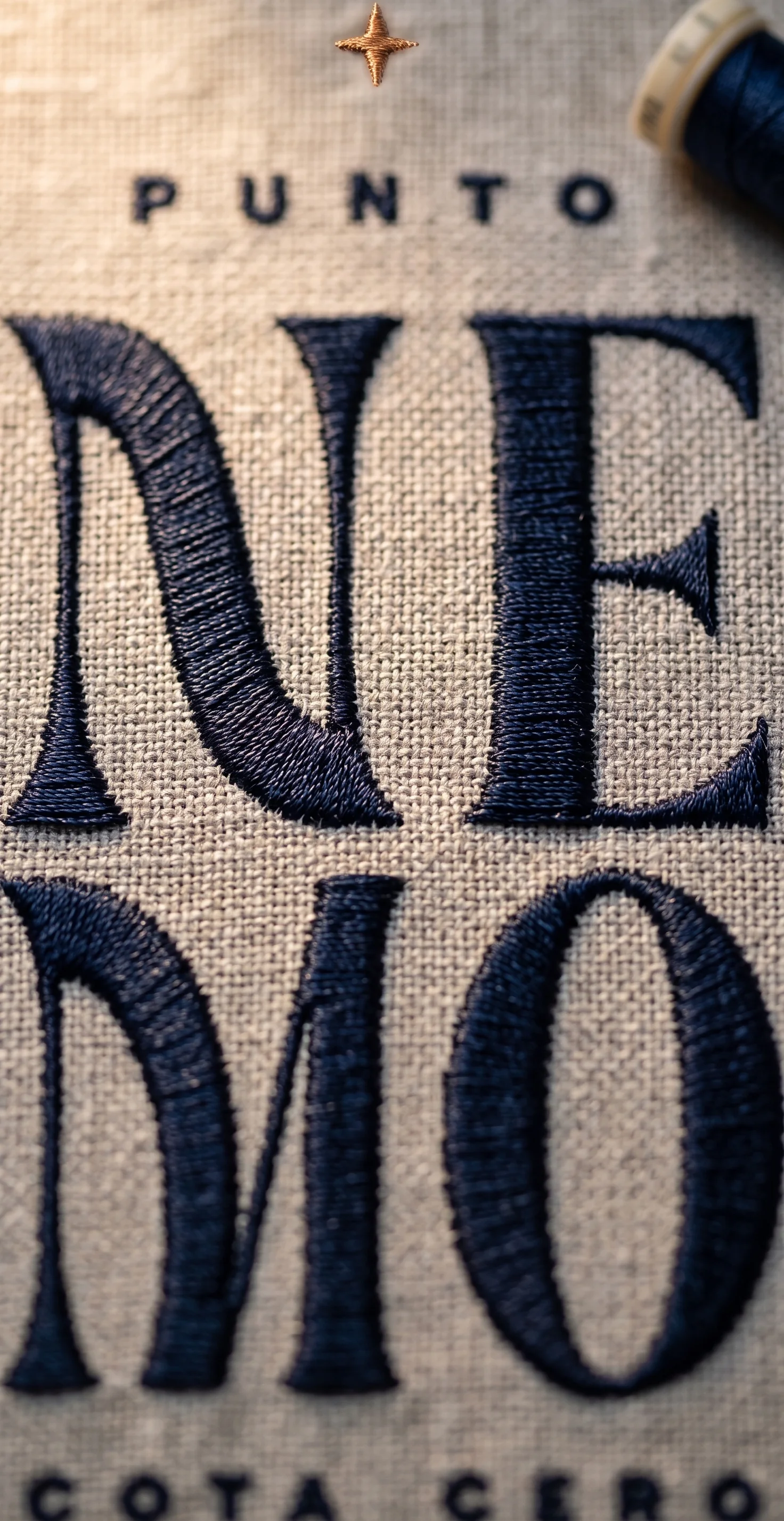 Bordado en hilo azul marino del logotipo Punto Nemo Cota Cero sobre tela de lino, detalle macro